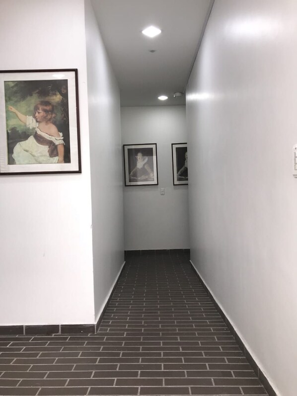 Un pasillo con piso de baldosas, paredes blancas y cuadros enmarcados.