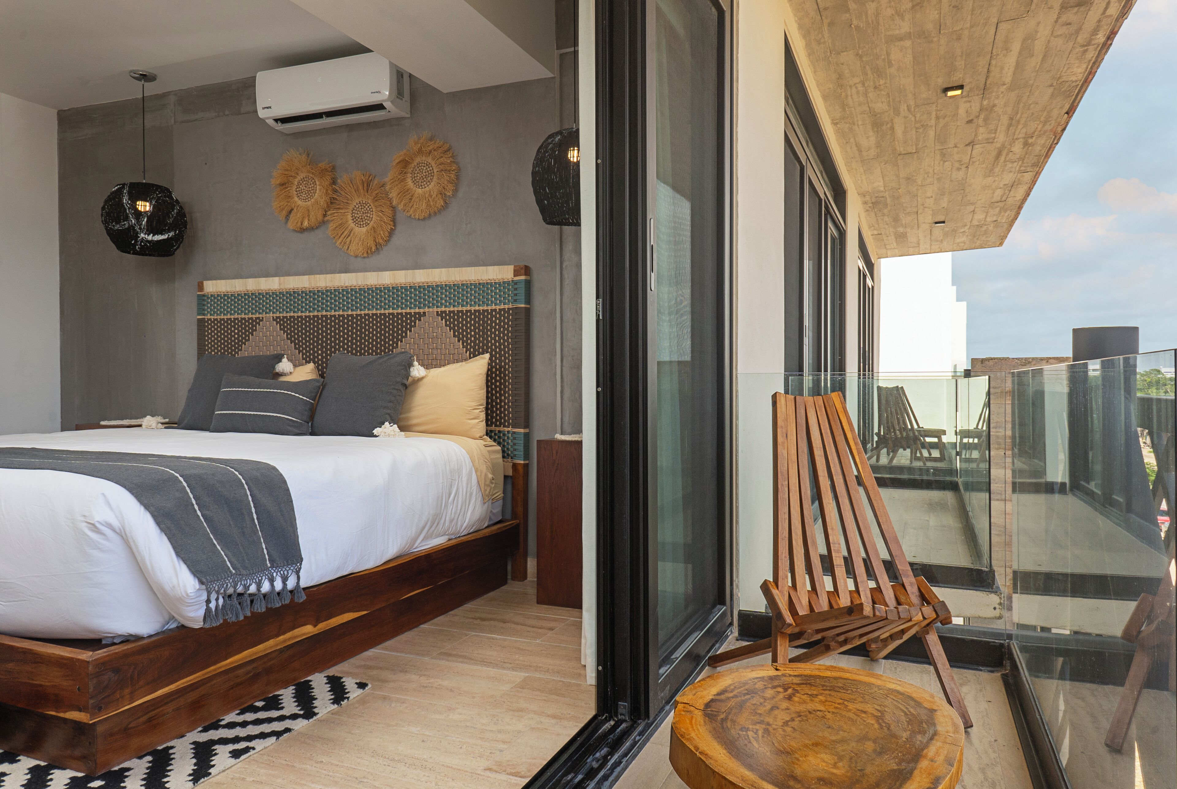 Une chambre moderne avec un grand lit, une chaise en bois et un balcon doté d’une balustrade en verre.