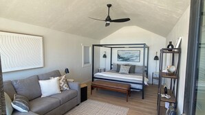 Une chambre à coucher moderne avec un lit, une table de chevet, une commode, un ventilateur de plafond, un canapé et un tapis à motifs.