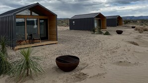Un paysage désertique parsemé de cabanes modernes et minimalistes, dotées de grandes fenêtres et de terrasses en bois.
