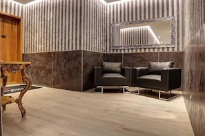 A modern lobby with a marble floor, a wooden reception desk, and two black leather chairs.