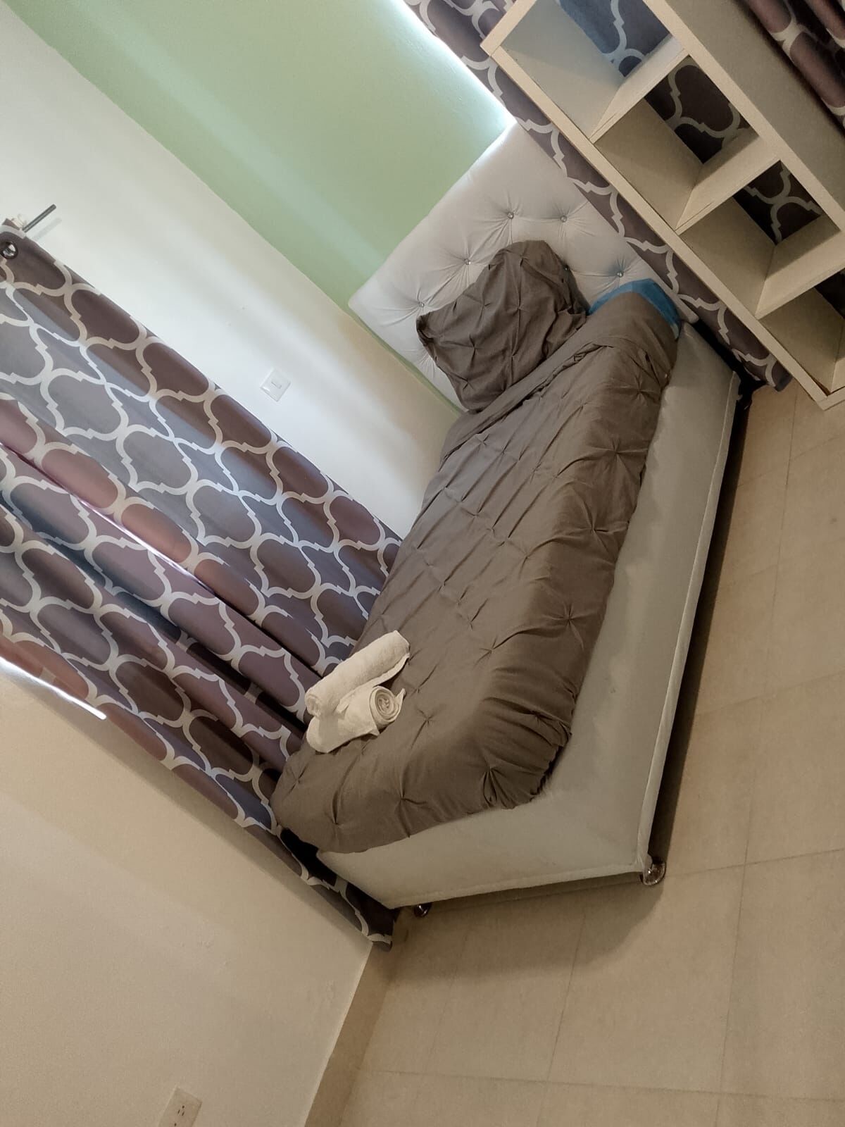A bed with a brown quilt and a rolled-up towel on it.