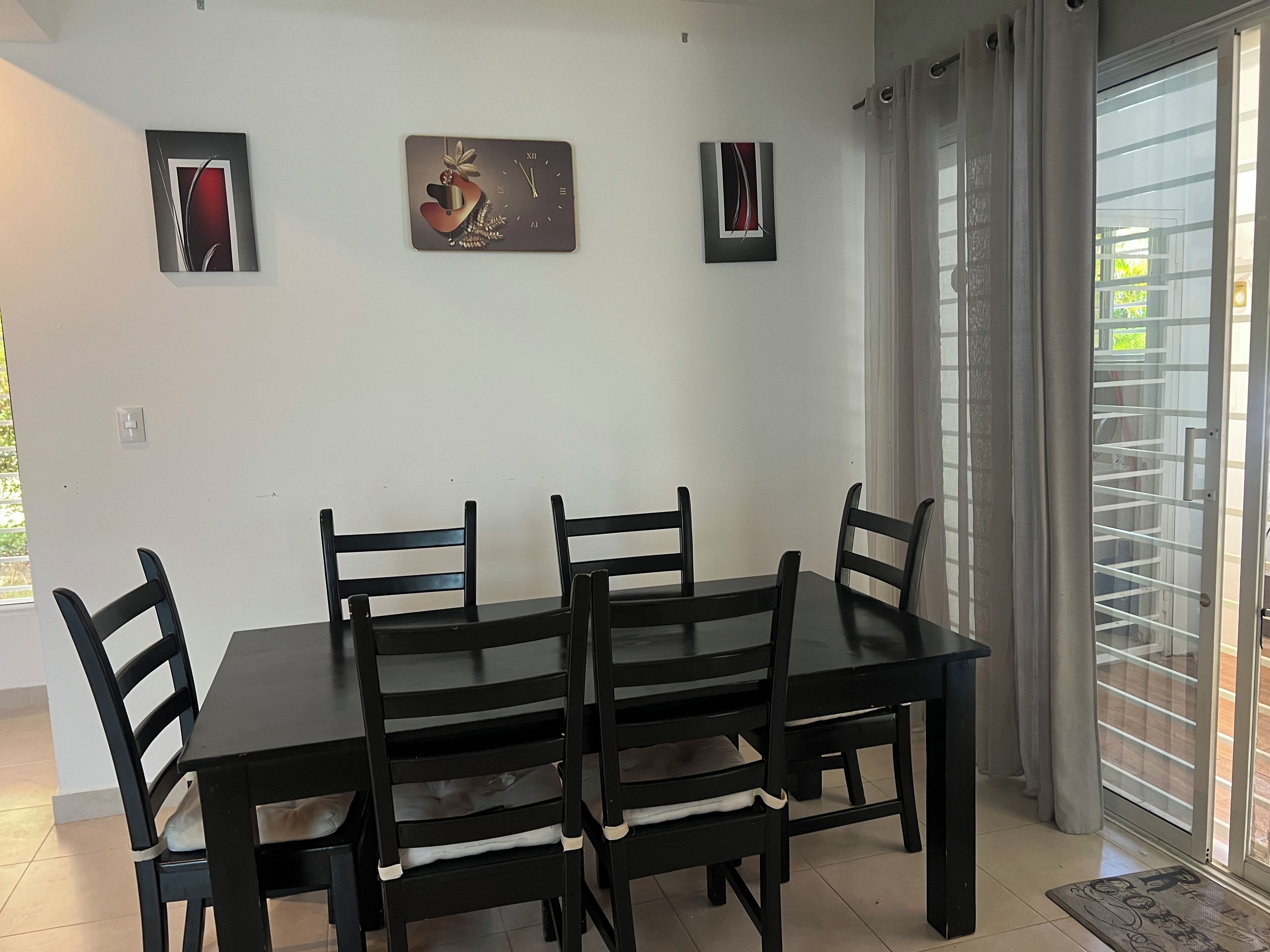 Un comedor con mesa y sillas de madera oscura, un reloj moderno y dos pinturas abstractas en la pared.