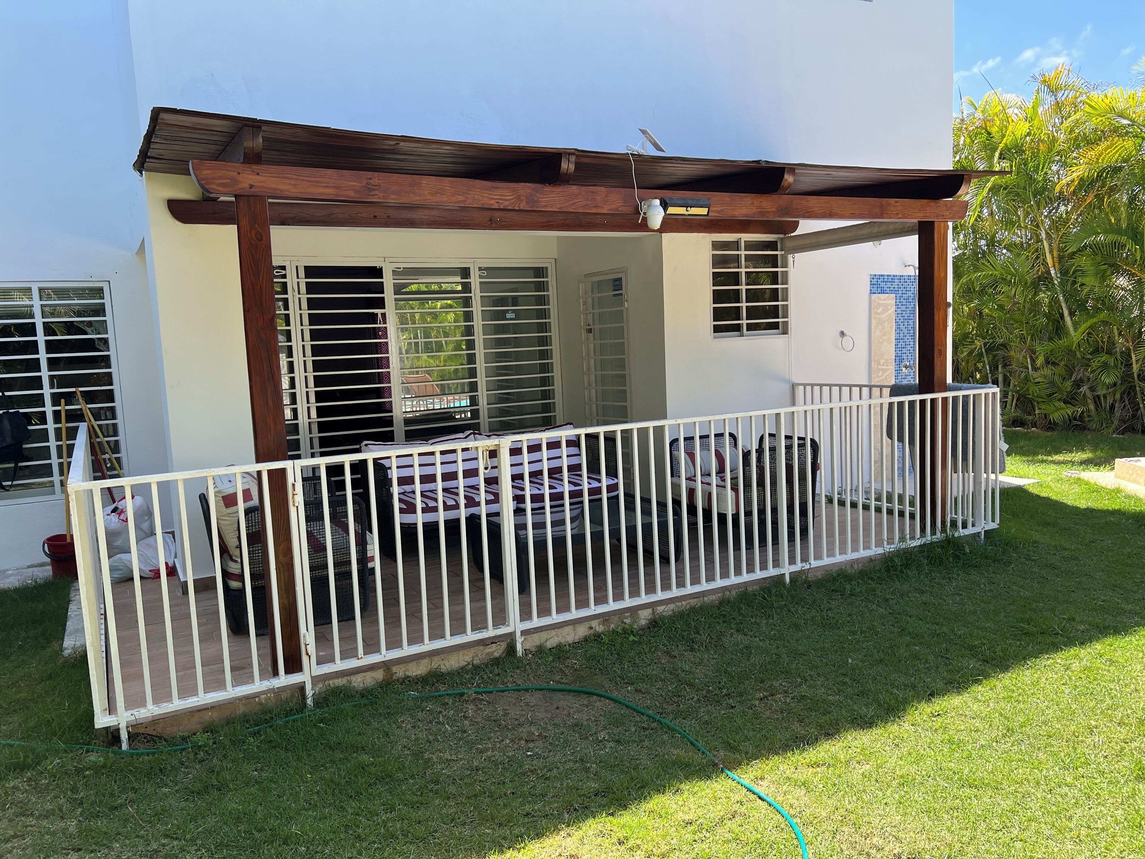 Ein überdachter Außenbereich mit weißer Brüstung, einer Holzpergola und Blick auf ein Gebäude mit großen Fenstern.
