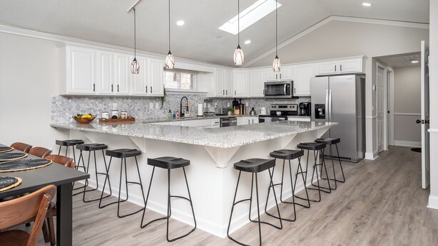 A modern kitchen with white cabinets, a large island with bar stools, and stainless steel appliances. - Lakefront Getaway: Fire Pit ~ Dock ~ Games ~ Family & Pet Friendly (Waterloo)