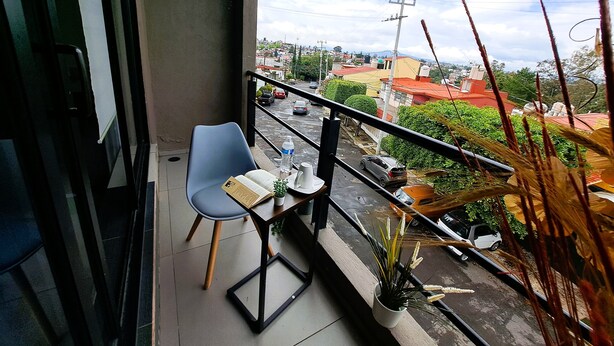 A balcony with a blue chair, a table with a book, a water bottle, and a potted plant.