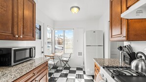 A kitchen with wooden cabinets, a microwave, a refrigerator, a stove, and a window with a view of palm trees. - NEW Private Ocean Beach Home with Yard and Parking (San Diego)