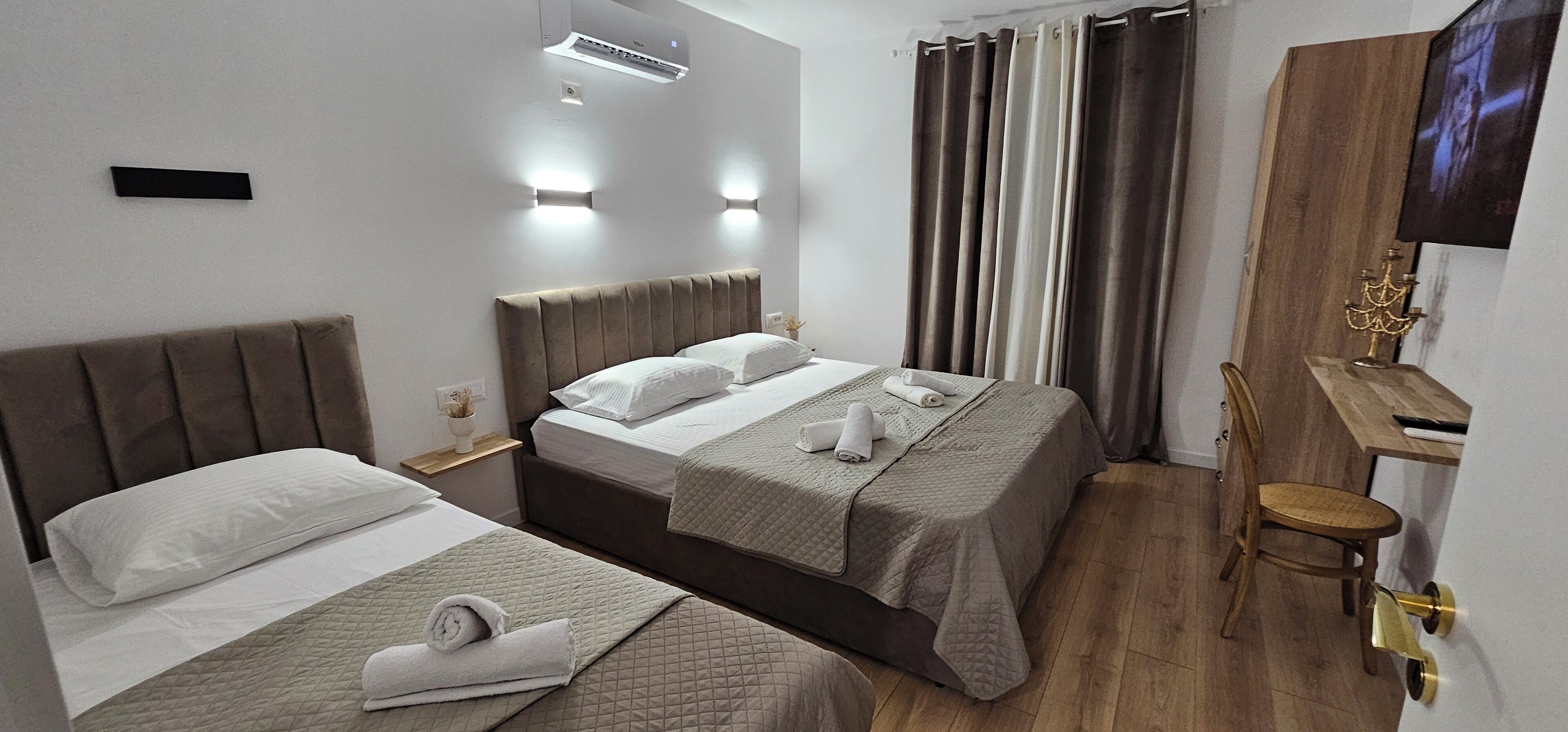 Habitación de hotel con dos camas, un escritorio, una silla, un televisor y aire acondicionado instalado en la pared.