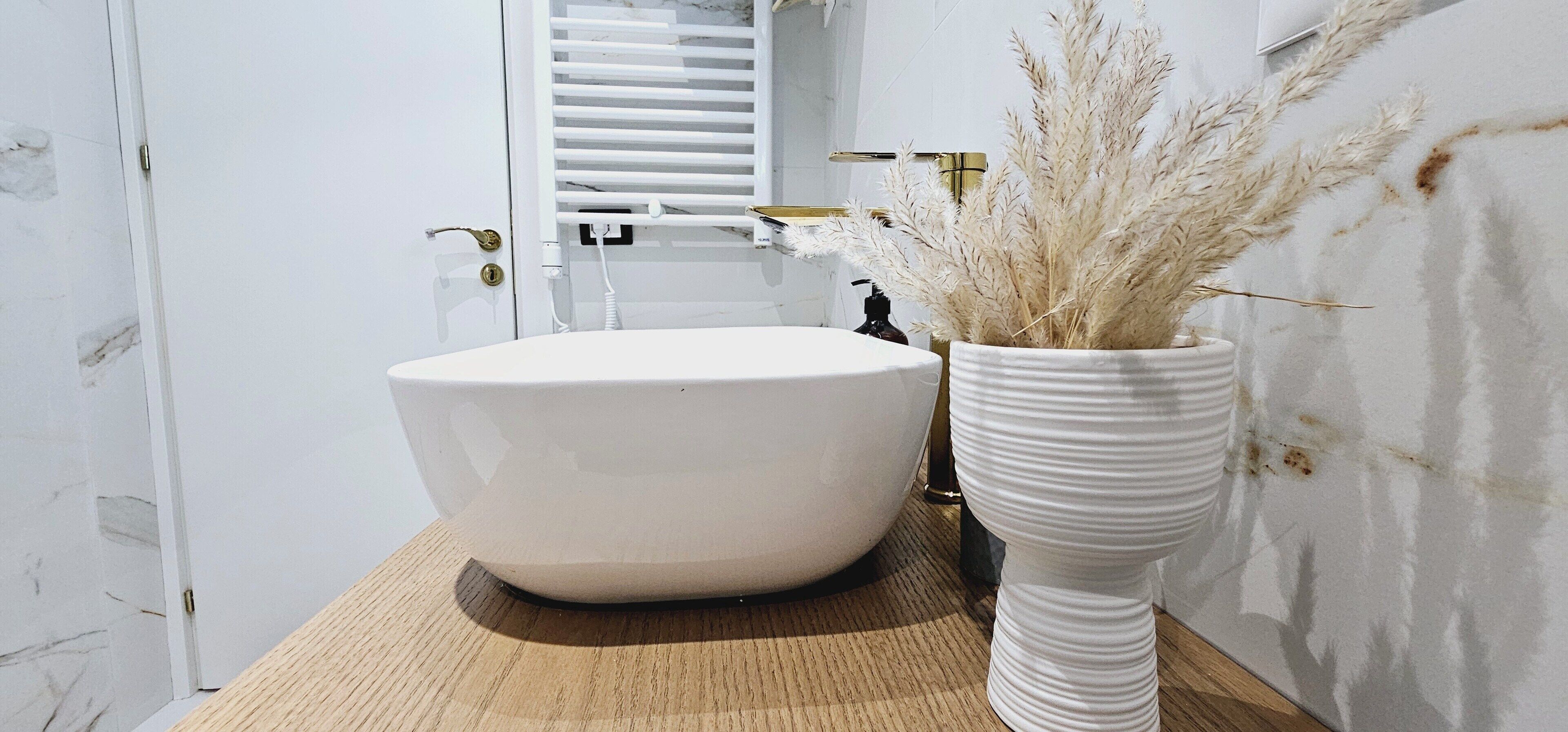 Un bany amb un gran lavabo blanc, un taulell de fusta i un vas blanc amb plantes seques.
