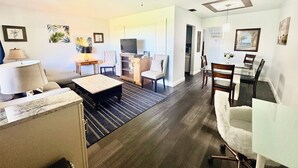 A modern living room with a sofa, coffee table, and TV. There is a dining area with a table and chairs. The room has hardwood flooring and a ceiling fan. - East Haven Tropical Escape. Off Atlantic Ave!! (Delray Beach)