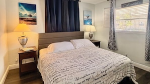 Een slaapkamer met een bed, twee nachtkastjes, een plafondventilator en een raam met gordijnen.
