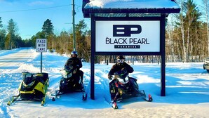 A sign for 'The Black Pearl Paradise' with two snowmobiles parked in front.