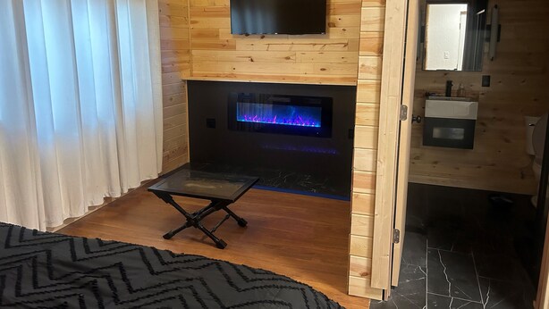 A wooden cabin interior with a fireplace, a television mounted above it, and a small table.