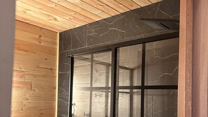 A bathroom with a wooden ceiling, a toilet, and a shower area with a black glass door.