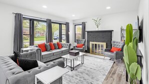 A modern living room with a grey sofa set, a fireplace, and large windows. - Roomy Retreat–Family&Friends|2 King Beds|Game Room | Valpo University | Dunes (Chesterton)