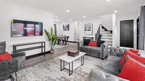 A modern living room with a grey sofa, a coffee table, and a TV mounted on the wall. - Roomy Retreat–Family&Friends|2 King Beds|Game Room | Valpo University | Dunes (Chesterton)