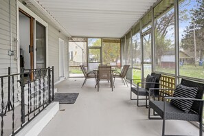 A covered porch with a table and chairs, a bench, and a view of the backyard. - Roomy Retreat–Family&Friends|2 King Beds|Game Room | Valpo University | Dunes (Chesterton)