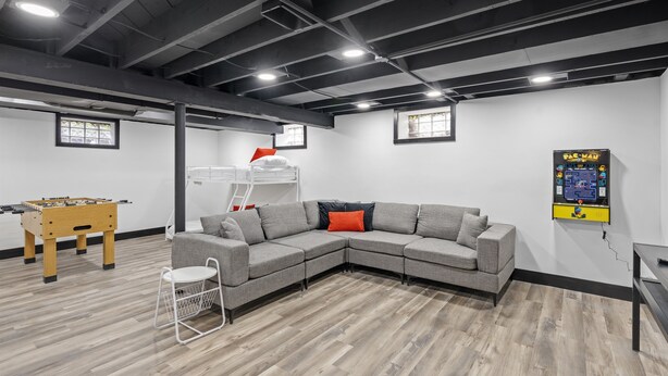 A modern living room with a sectional sofa, a foosball table, and a wall-mounted TV. - Roomy Retreat–Family&Friends|2 King Beds|Game Room | Valpo University | Dunes (Chesterton)