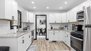 A modern kitchen with white cabinets, a stainless steel refrigerator, a microwave, a stove, and a dining area with a table and chairs. - Roomy Retreat–Family&Friends|2 King Beds|Game Room | Valpo University | Dunes (Chesterton)