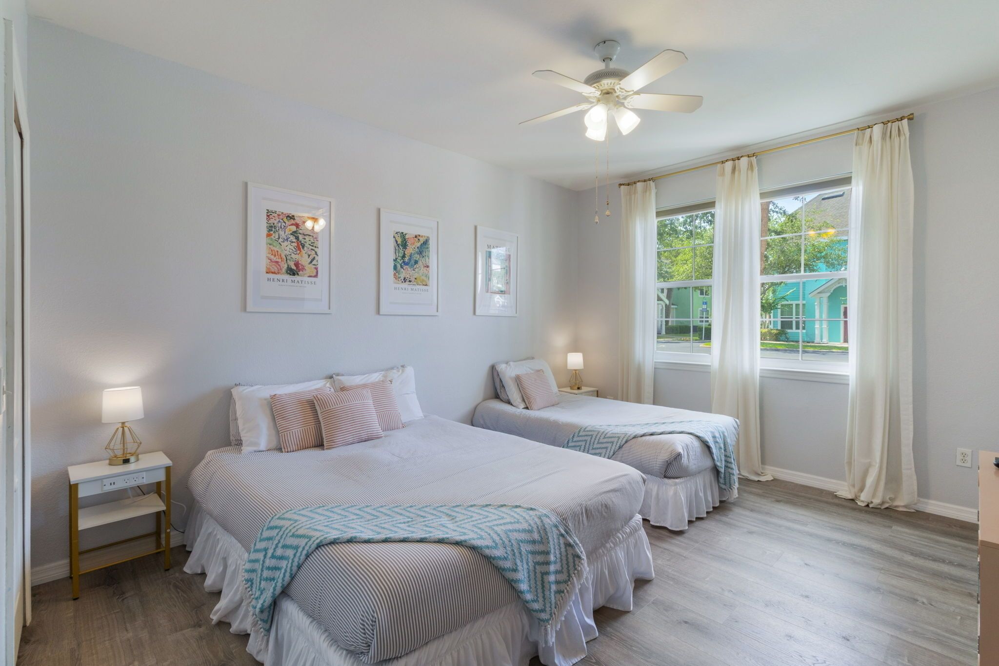 A bedroom with two beds, a ceiling fan, and a window with curtains.