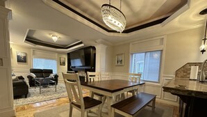 A dining area with a wooden table and chairs, a chandelier, and a television above the fireplace. - Sumner Park Residence (Rochester)