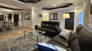 A modern living room with a glass coffee table, a black leather sofa, and a patterned rug. - Sumner Park Residence (Rochester)