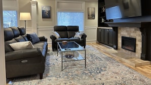 A living room with a fireplace, a sofa, a coffee table, and a TV mounted on the wall. - Sumner Park Residence (Rochester)