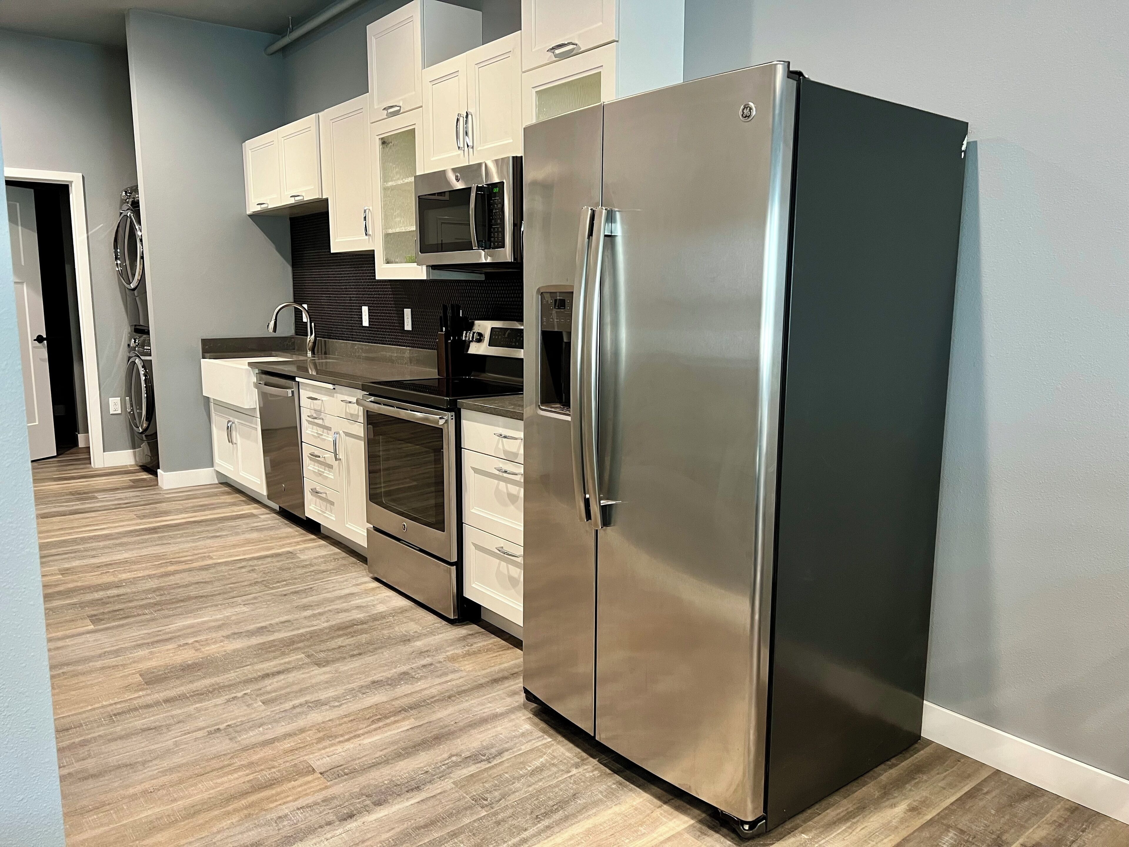 A modern kitchen with stainless steel appliances, white cabinetry, and a wooden floor.