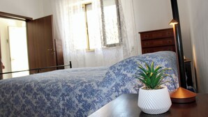 Ein Schlafzimmer mit einem Bett, einem Nachttisch mit Topfpflanze, einer Kommode und einer Lampe.