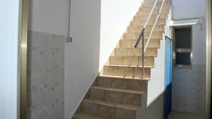 Eine Treppe mit beigen Fliesen, einem Metallgeländer und einem kleinen Fenster mit blauer Vorhang.