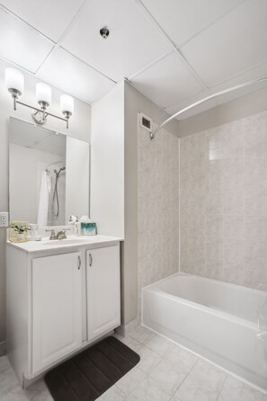 Bathroom features a white vanity with a mirror, sink, and towel rack, alongside a bathtub with a showerhead.