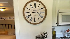 Una cocina con armarios blancos, una estufa y un microondas. Hay un mueble de madera con un reloj encima.