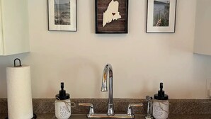 Una cocina con un lavamanos de acero inoxidable, dos dispensadores de jabón y tres cuadros en la pared.