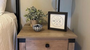 Una mesita de noche de madera con una lámpara, un cuadro enmarco, un tazón y una planta en maceta.