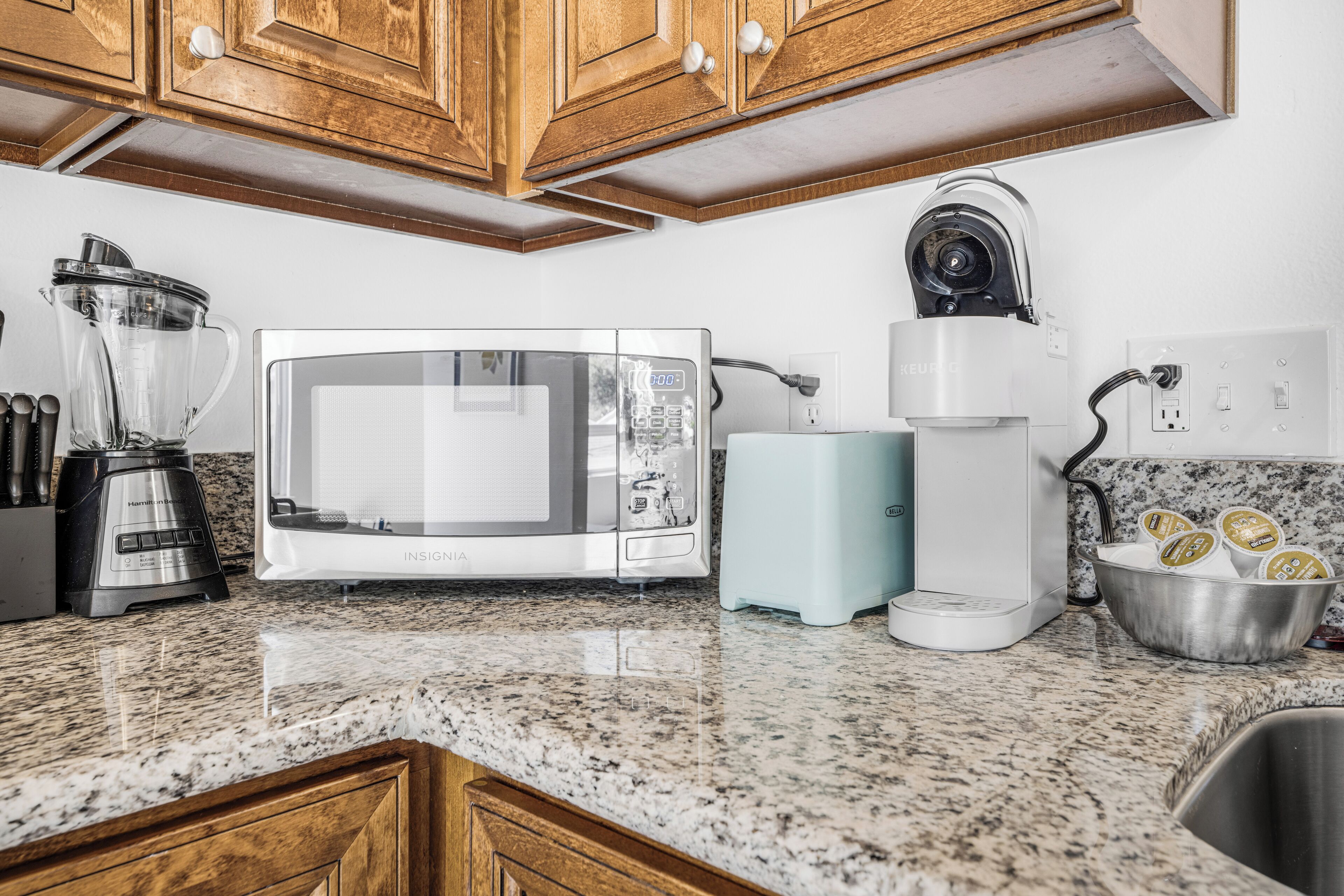 Una cocina con microondas, cafetera, licuadora y un tazón de yogur.