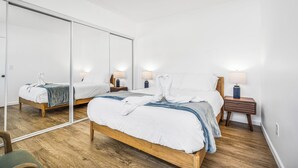 A bedroom with a wooden bed, two bedside tables with lamps, a large mirror, and a wooden floor. - NEW 1br Ocean Beach Apartment w/ Parking - Short Walk to the Beach (San Diego)