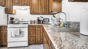 A kitchen with wooden cabinets, a white stove, a microwave, and a granite countertop. - NEW 1br Ocean Beach Apartment w/ Parking - Short Walk to the Beach (San Diego)