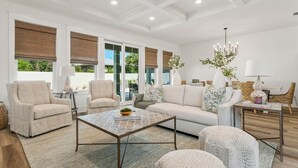 A spacious living room with a sofa, armchairs, a coffee table, and a chandelier. - Exceptional New Build - West End - Pool - Golf Cart (Panama City Beach)