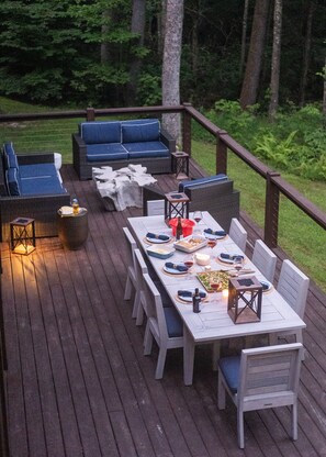 A deck with a dining table set for six, surrounded by wicker furniture and a sofa. - BEAR'S DEN  - Spacious mountain home on river game room & fire pit in Burlingame (Sapphire)
