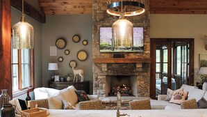 A cozy living room with a stone fireplace, a marble island with a sink, and a large TV mounted above the fireplace. - BEAR'S DEN  - Spacious mountain home on river game room & fire pit in Burlingame (Sapphire)
