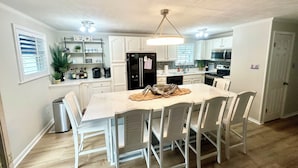 A modern kitchen with white cabinetry, a central island with chairs, and a ceiling fan.