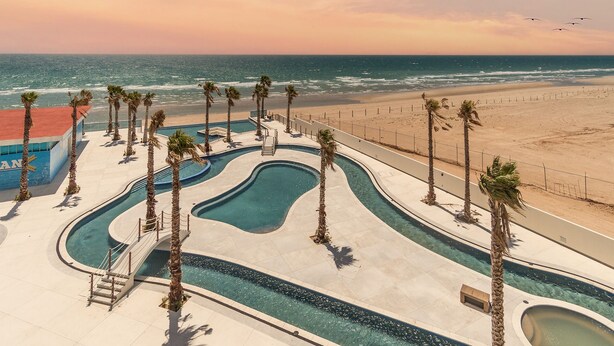 Un resort con varias piscinas, palmeras y vista al mar.