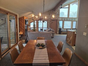A dining area with a wooden table, chairs, and a chandelier. There is a Christmas tree and a fireplace in the background. - Lake-Golf-Ski condo  w/ great views & boat parking (Mancelona)