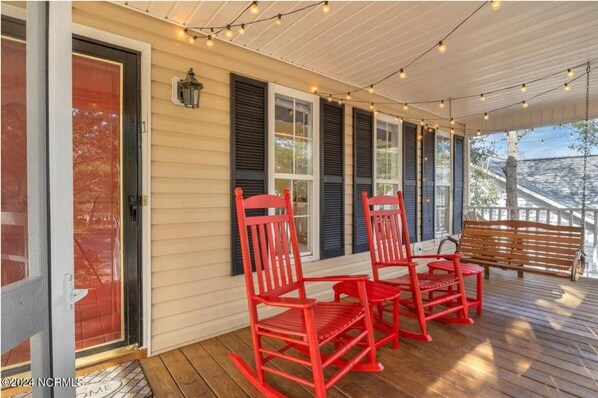 A covered porch with a wooden bench and two red rocking chairs. - 5 mins to beach, golf cart & fenced in yard. Pet-friendly! (Oak Island)