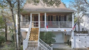 A two-story house with a front porch, a staircase, and a garage. - 5 mins to beach, golf cart & fenced in yard. Pet-friendly! (Oak Island)