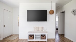 Ein modernes Wohnzimmer mit einem großen Flachbildfernseher an einer weißen Wand, einer Sitzbank mit Stauraumbetten und einer Pendelleuchte.