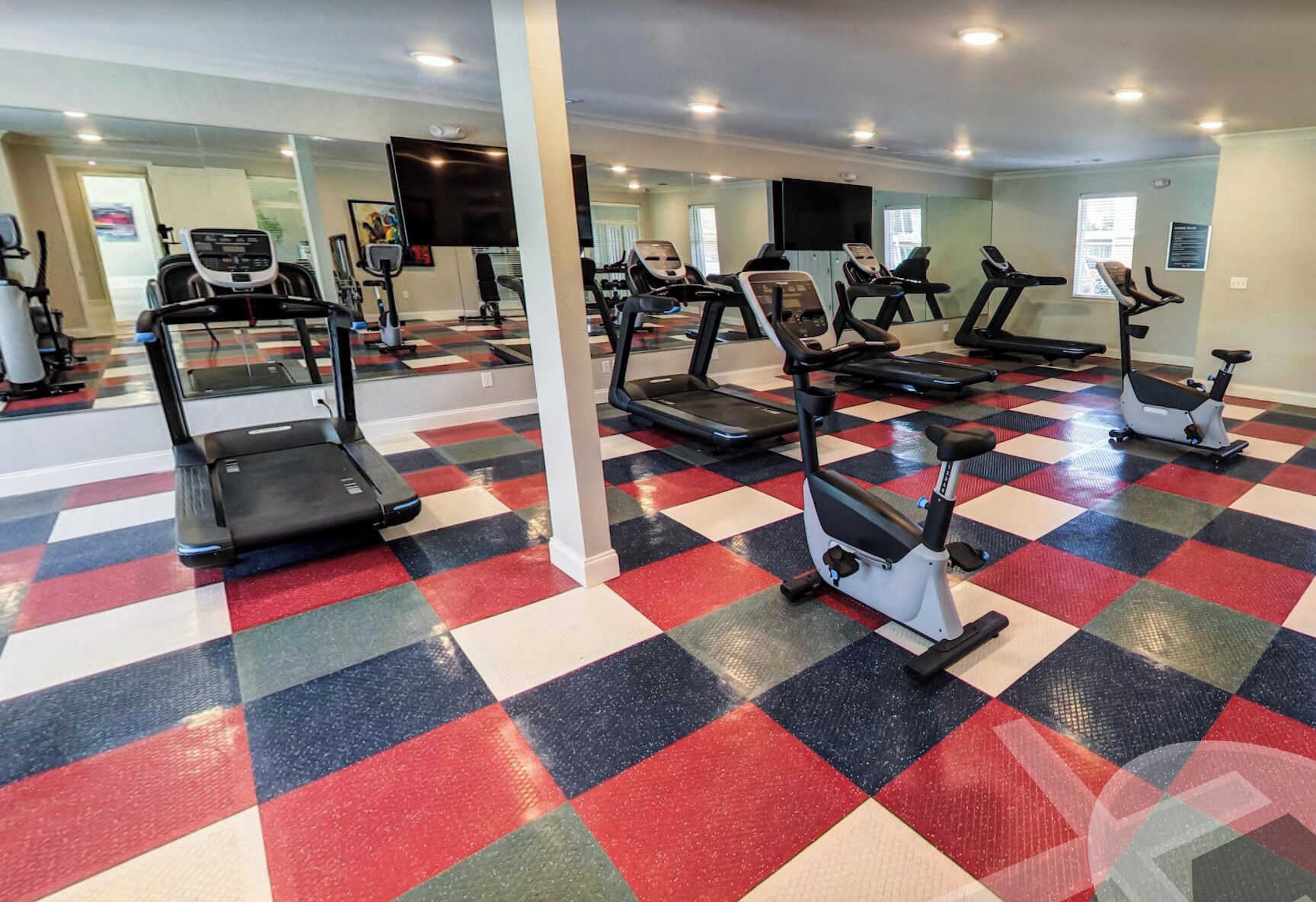 Ein Fitnessraum mit mehreren Laufbändern und Ergometer, einem Schachbrettmuster-Boden und einem großen Spiegel.