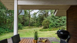 Um deck de madeira com mesa, cadeiras, churrasqueira e um vaso de planta.