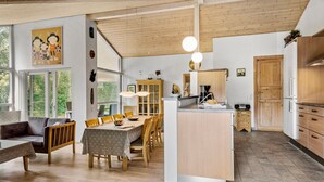 Uma sala de estar ampla com mesa de jantar, móveis de madeira e cozinha equipada com eletrodomésticos modernos.