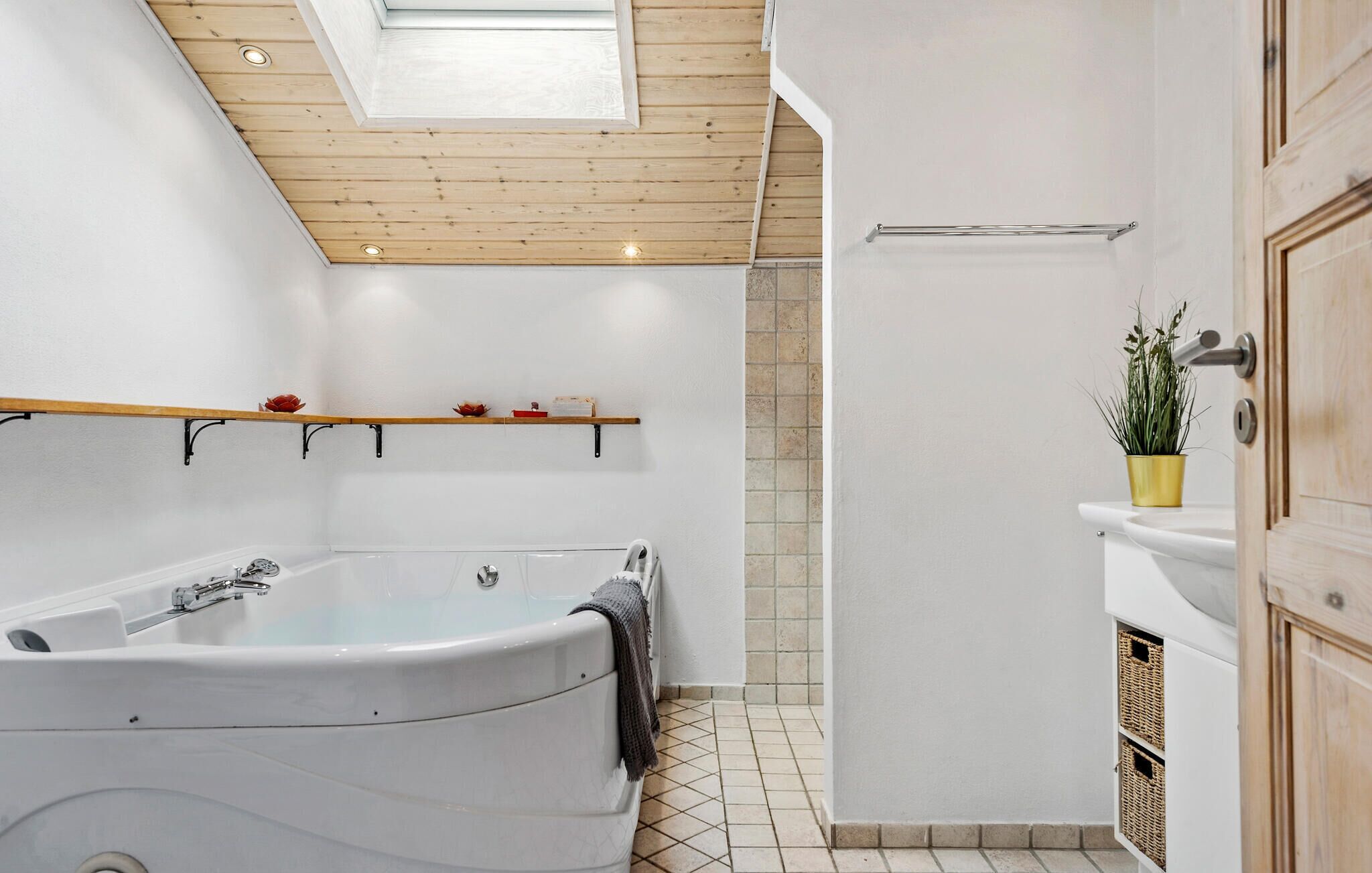 Un baño moderno con una bañera independiente, techo de madera y una pequeña estantería con adornos.